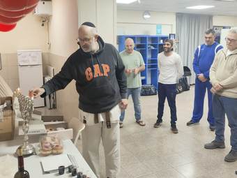חבר הדוג'ו מדליק נר בחנוכייה על שולחן עם סופגניות בעוד קבוצת מתאמנים עומדת ומתבוננת